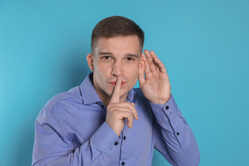 Man showing hand to ear gesture on light blue background