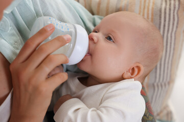 Mother feeding her cute baby indoors, closeup