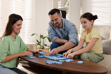 Fototapeta premium Happy parents and their daughter solving puzzle together at wooden table indoors