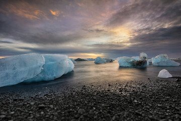 Blue icebergs on black sand beach at twilight. Breathtaking winter seascape with drifting ice formations at the edge of Arctic waters. © fegari