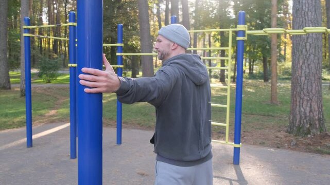 Man stretches hands preparing to workout at outdoor gym. Athlete is warming up, ready to train in the park on a sunny day