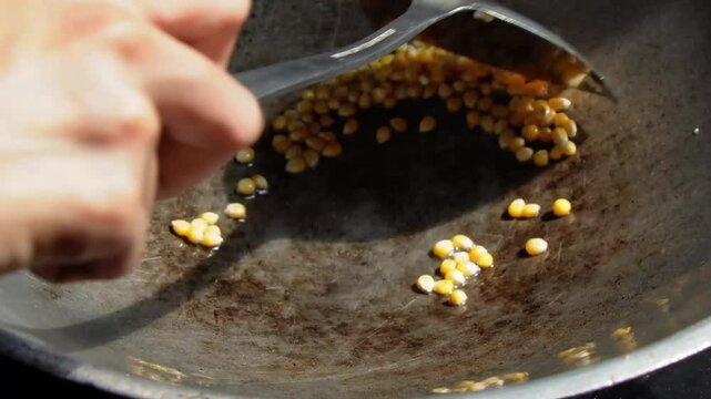 A close-up shot of popcorn kernels being stirred in a wok. Homemade popcorn preparation. A Step-by-Step Guide of Making Homemade Popcorn.