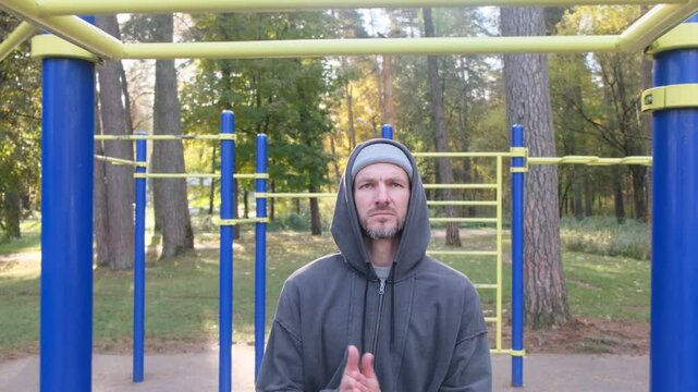 Man in a hooded jacket standing near workout bars in park. Exercise, fitness, outdoor lifestyle, healthy concept