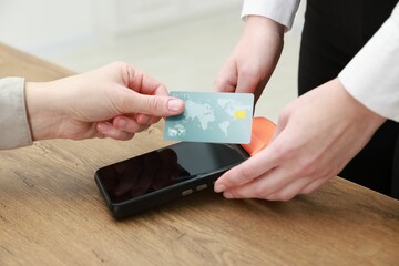 Woman paying for service with credit card via terminal at wooden table indoors, closeup