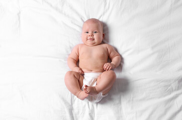 Cute little baby in diaper on bed, top view