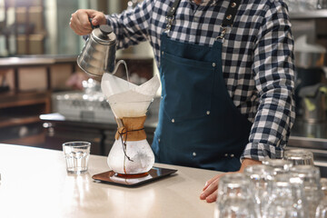 Barista brewing coffee in glass coffeemaker with paper filter at table in cafe, closeup