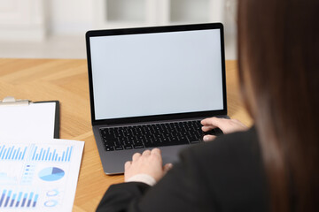 Businesswoman working with laptop at wooden table in office, closeup
