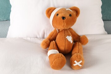 Cute teddy bear with bandages, adhesive medical plasters and thermometer on bed