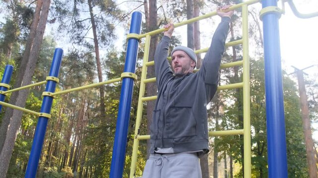 Man doing pull-ups on outdoor gym equipment. Trees and sky background. Active lifestyle. Workout in the park