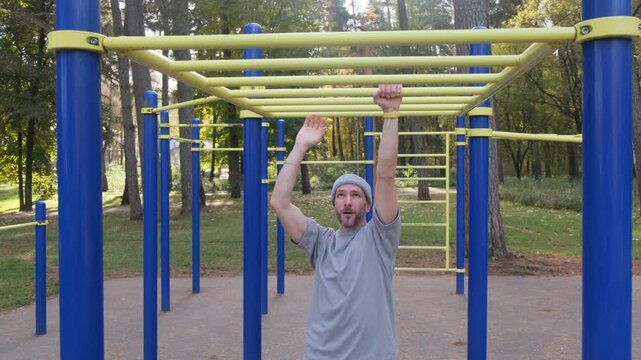 Man moves along monkey bars in outdoor gym. Strength training. Active, healthy lifestyle