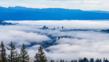 High-rise buildings poking through cloud inversion over valley with mountains in silhouette on...
