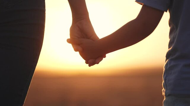 A person holding hands in the sunset. Mom, holds, daughter, hands walk, park. Mom and daughter walking in the park. The photo is of a mother and child holding hands at lifestyle sunset.