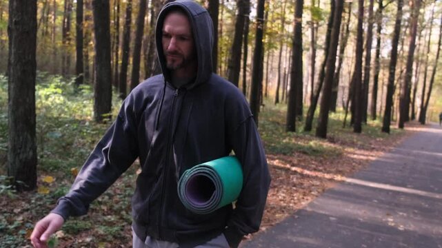 Man with a yoga mat walking through an autumn forest