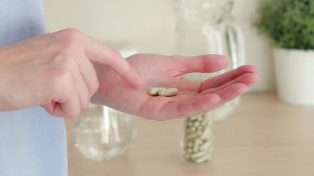 Close-up of a woman holding two gray pill capsules in her hand