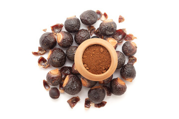 A mud pot filled with organic Soapnuts or Reetha (Sapindus mukorossi) powder, placed on a heap of Soapnuts berries, isolated on a white background.