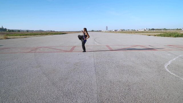 Chica practicando artes marciales en el paisaje infinito y minimalista de una pista de aterrizaje un d&iacute;a soleado con cielo azul.
