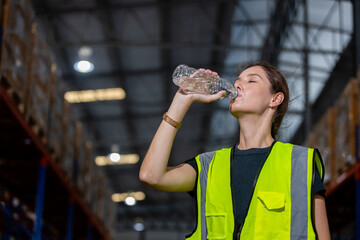 Women engineer drinking water from plastic bottle after working at factory during break. Drinking...