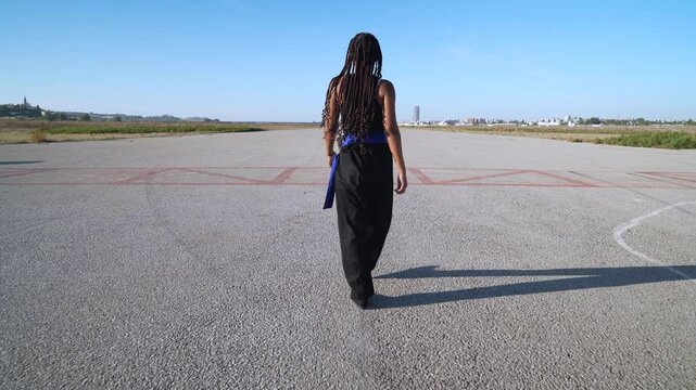 Chica luchadora en artes marciales que sale del objetivo es seguida hasta que se para, se pone en guardia, saluda y combate. Hasta que se para, saluda y anda hacia la c&aacute;mara.