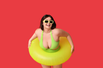 Beautiful young woman in swimsuit with inflatable ring on red background