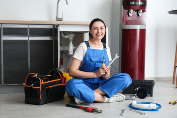 Female plumber with tools sitting near sink in kitchen