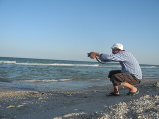 person watching the sea person on the beach photographer at sea takes pictures of nature and people street photos and videos walks along the seashore and beach in a vest with a camera you can see the 
