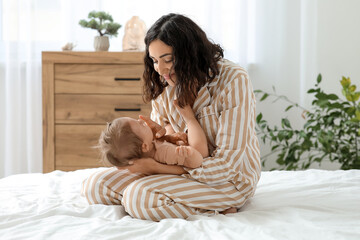Happy mother with her little baby sitting on bed at home