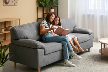 Obraz premium Beautiful young happy Asian mother and cute little daughter reading book at home