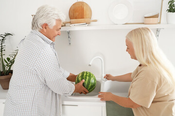 Mature couple washing fresh watermelon in kitchen