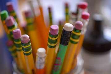 “Close-up of a collection of sharpened pencils arranged in a circular pattern, showcasing fine details and textures of the wooden bodies, graphite tips, and colorful erasers. 