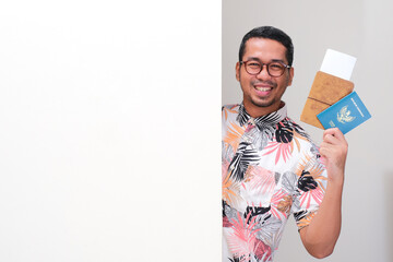 A tourist peeking behind wall smiling happy holding travel document, ticket and indonesia passport