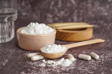 Bowl, wooden spoon with collagen powder and pills on grey grunge background