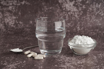 Glass of water, bowl, spoon with collagen powder and pills on grey grunge background