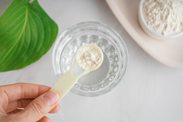 Female hand holding scoop with collagen powder on white background