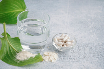 Glass of water, bowl with pills and collagen powder on white grunge background