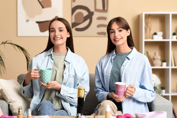 Young sisters with cups of tea and makeup products recording podcast at home