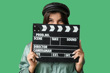Young thoughtful female film director with movie clapper on green background