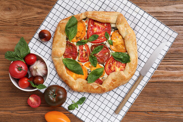 Composition with tasty tomato galette, ingredients and knife on wooden background