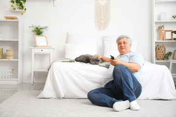 Senior man with cute cat watching TV in bedroom