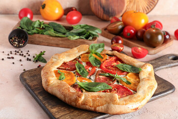 Wooden board of tasty tomato galette with basil and peppercorn on beige background