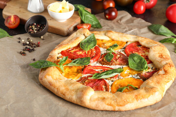 Baking paper of tasty tomato galette with basil and peppercorn on black background, closeup