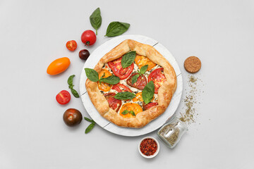 White board of tasty tomato galette with basil and spices on grey background