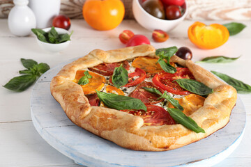 Board of tasty tomato galette with basil on white wooden background