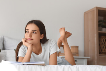 Fototapeta premium Beautiful young thoughtful woman reading book on bed at home