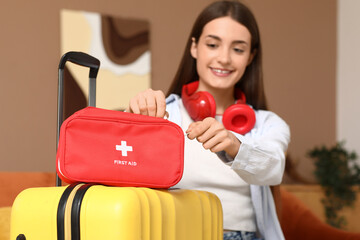 Young happy woman with suitcase, headphones and first aid kit at home. Travel concept