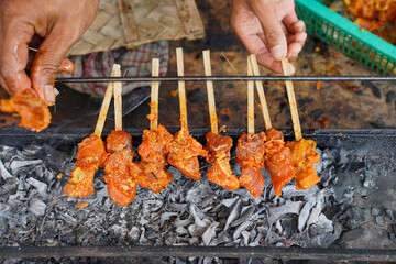 Close-up of traditional pork satay skewers being grilled over hot charcoal, showcasing authentic Indonesian street food preparation and vibrant flavors of Balinese cuisine