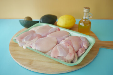 Fresh Chicken Thighs with Avocados and Lemon on Wooden Cutting Board