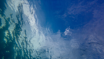 View from underwater to the sea surface. View from the bottom of the sea to the sky with clouds through the clear transparent thickness of water.