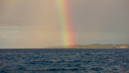 Rainbow over the sea. A rainbow column rises up from the surface of the sea against the backdrop of a tropical island.