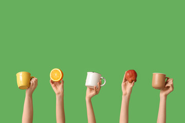 Female hands with orange, apple and mugs of tasty mulled wine on green background