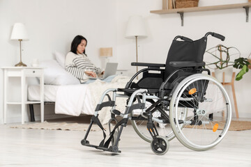 Beautiful young woman with wheelchair and laptop lying on bed at home